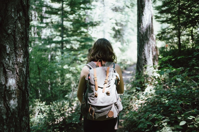 Girl wearing natural forests costume and carrying a bag of mountain hiking equipment, walking in the woods